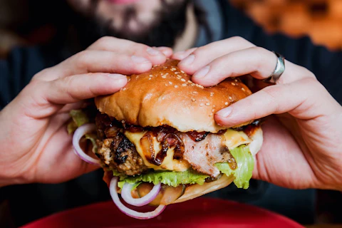 Zbliżenie na cheeseburgera trzymanego w dłoniach przez mężczyznę.